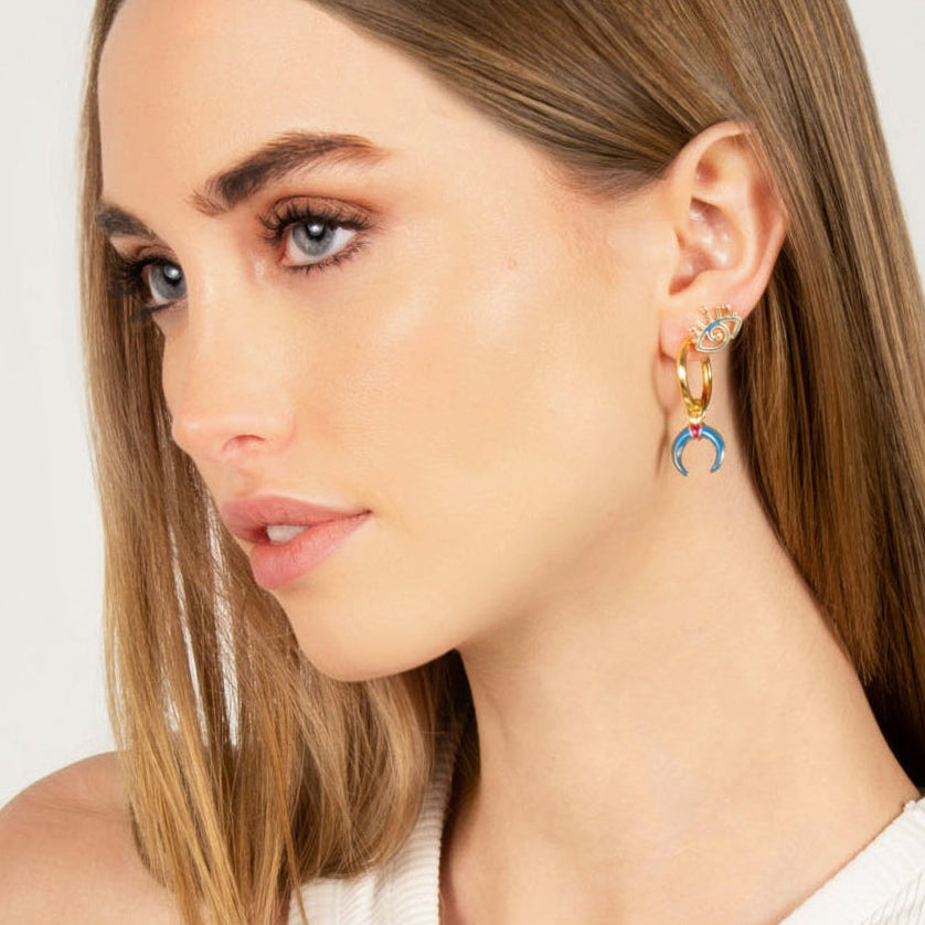Model wearing Gaia blue enamel hoop earrings with gold hoops and crescent charms.
